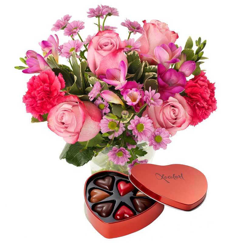Bukett med blommor i rosa och cerise; rosor, nejlikor, germini +en ask med chokladhjärtan. Gåvan finns att köpa hos Euroflorist.