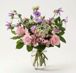 Somrig bukett med rosa rosor, lila clematis, prärieklockor och dekorationsgrönt. Blommorna hittar du i Interfloras egen onlinebutik. Gör någon glad med ett blomsterbud!