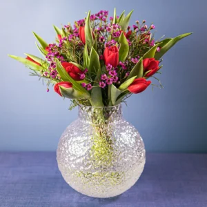 Euroflorists månadsbukett för februari, med röda tulpaner, lila vaxblommor och gröna blad.